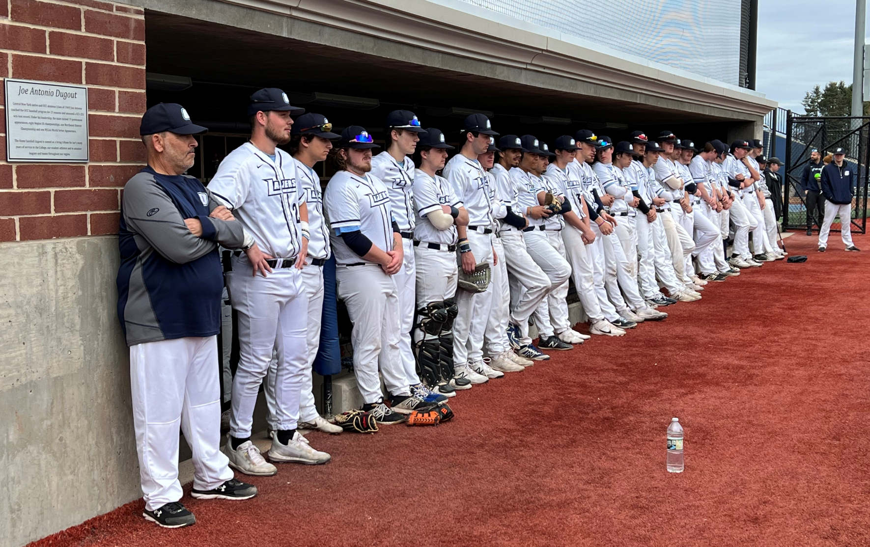 Players watched the ceremony while standing in front of the Joe Antonio dugout.