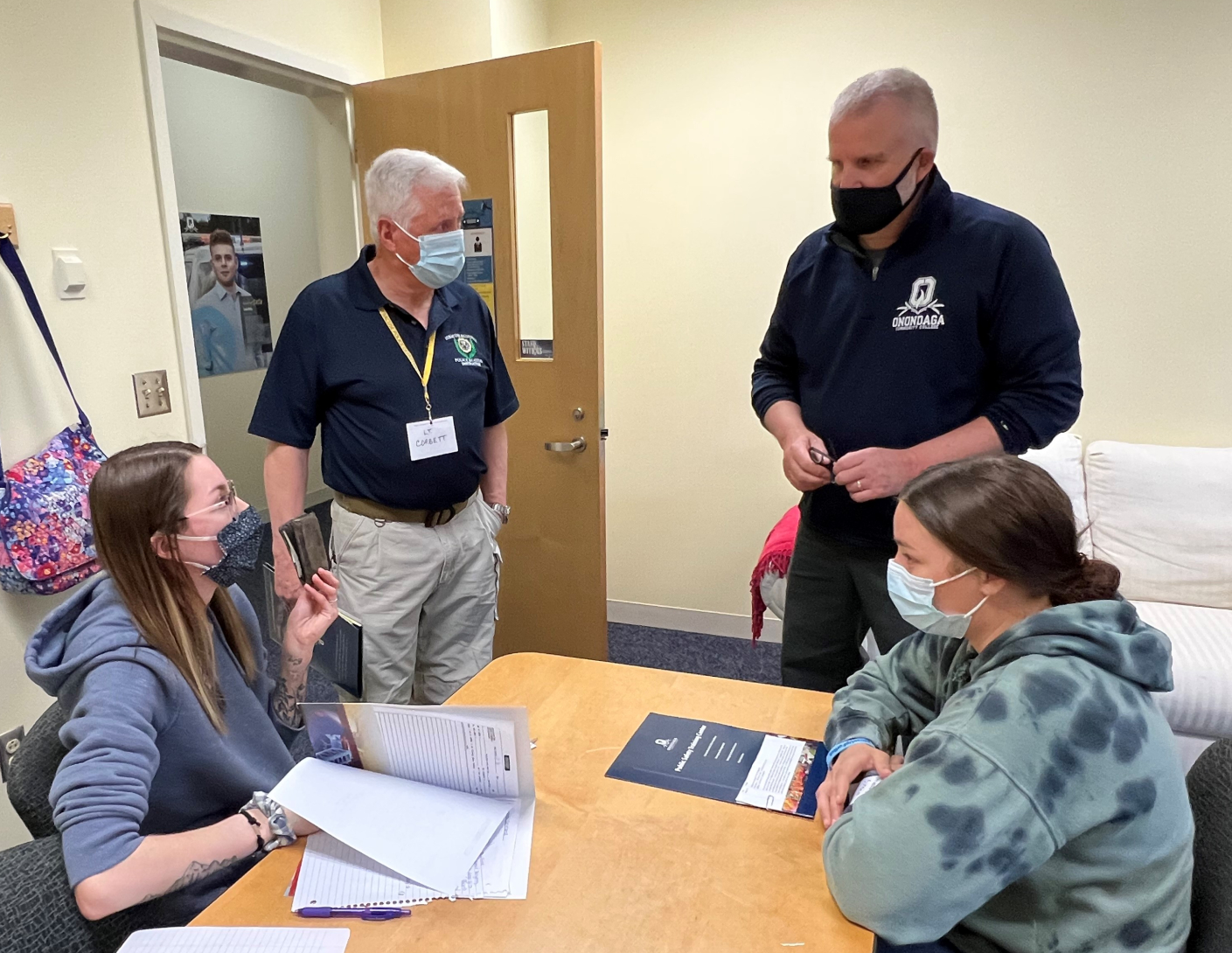 Investigator Miranda Cleveland (seated left) shows the wallet she found on the suspect, Julianna Barton (seated right). Standing are Lieutenant John Corbett (left) and Professor Pete Patnode (right).